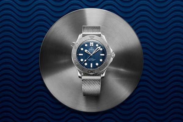 Omega Seamaster Diver 300M from the 007 series — blue wave dial on a Milanese mesh bracelet against a blue wave background